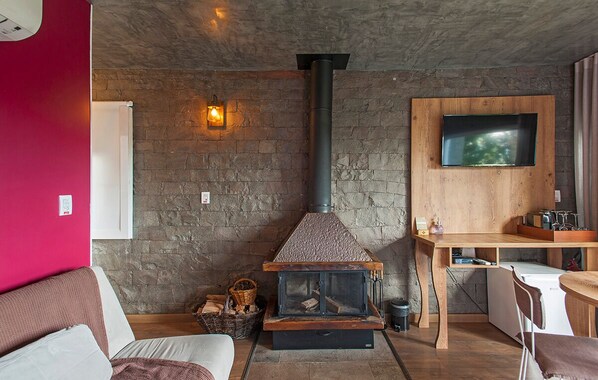 Uma sala de estar acolhedora com parede de pedra, lareira, televisão fixada na parede e um espaço de refeições com mesa e cadeiras.