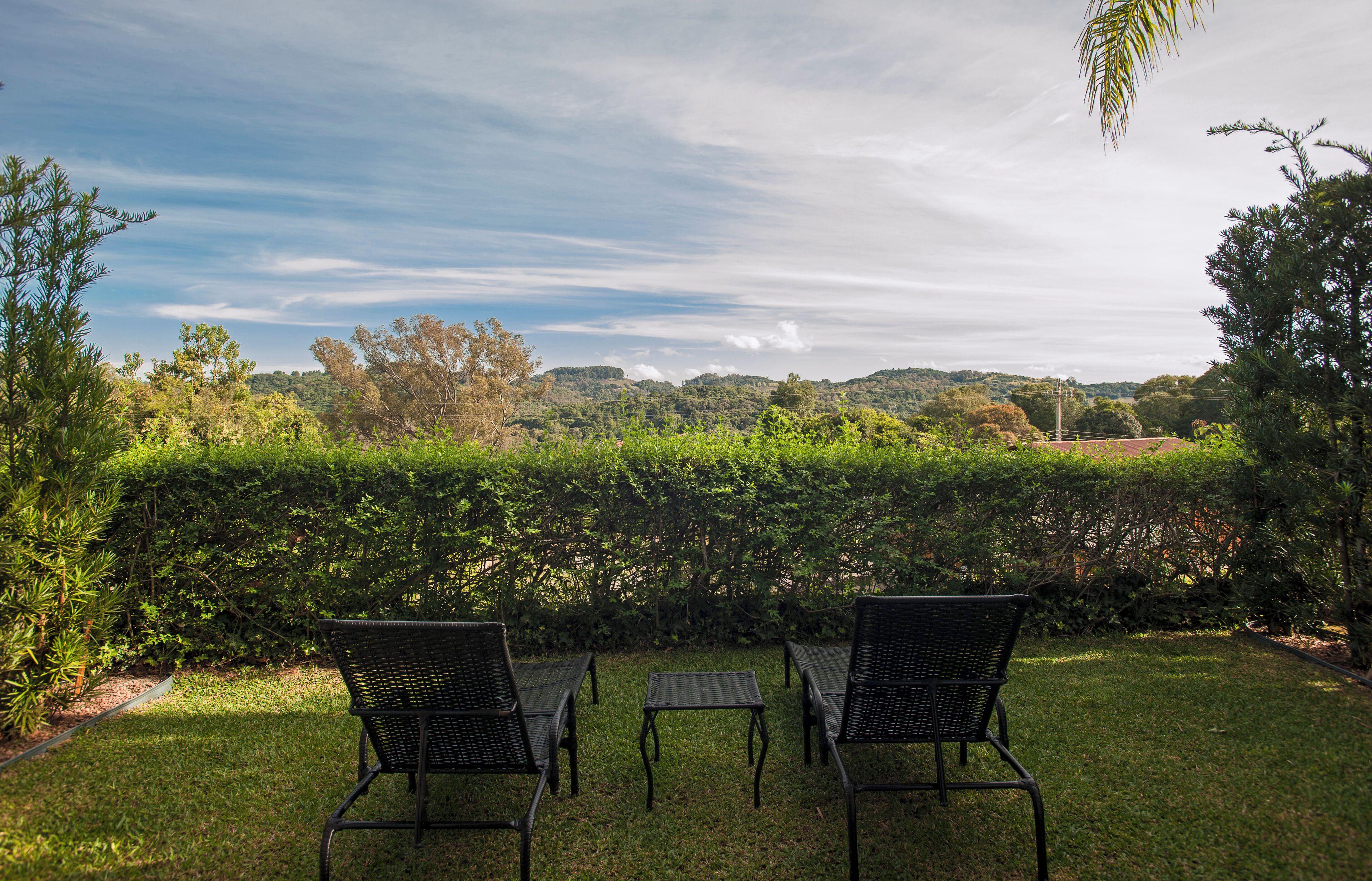 A patio with two chairs and a small table, surrounded by lush greenery and a view of distant hills.