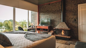 Une chambre moderne avec un grand lit, une télévision, une cheminée et une vue sur l’extérieur.