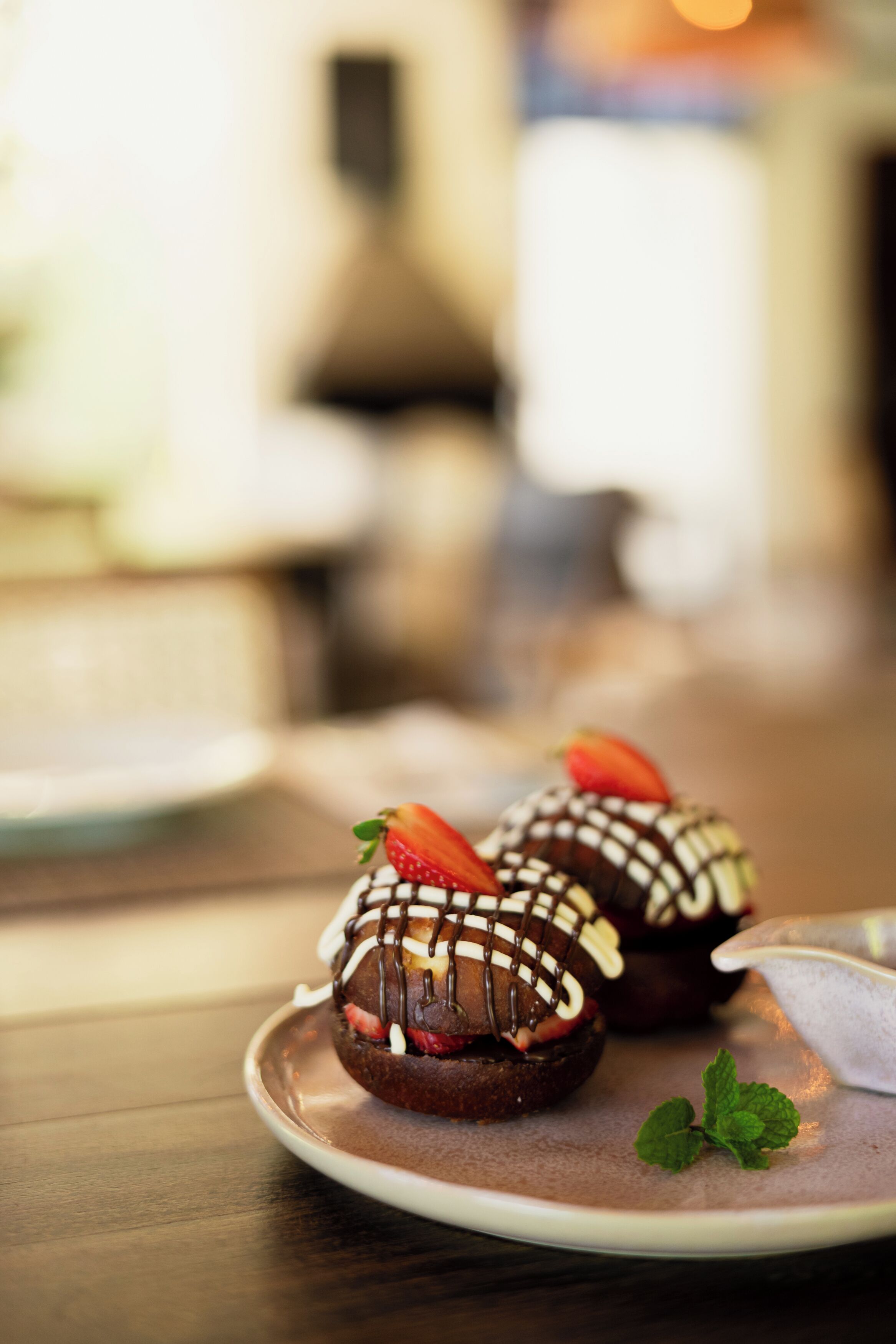A plate with two chocolate-covered pastries garnished with strawberries and mint leaves.