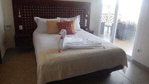 Quarto de hotel com uma cama grande, cabeceira de madeira e vista para o exterior através de uma porta de vidro deslizante.