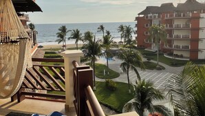 Varanda de hotel com vista para o oceano, palmeiras e área de piscina.