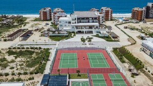 Um hotel à beira-mar com vários edifícios, uma quadra de tênis e uma praia ao fundo.
