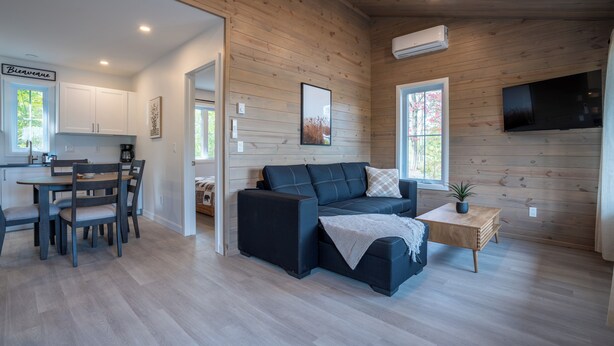 Un interior moderno con techo de madera, comedor, sofá y televisor montado en la pared.