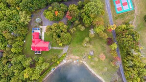 Vista aérea de una propiedad con un edificio de techo rojo, cancha de tenis y un lago.