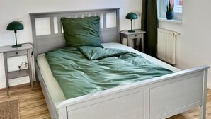 Ein Schlafzimmer mit einem Bett, zwei Nachttischen, einem Fenster mit Vorhängen und einer Heizung.
