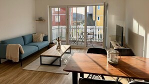 Ein modernes Wohnzimmer mit einer Couch, einem Holzesstisch und einem Balkon mit Blick auf Gebäude.