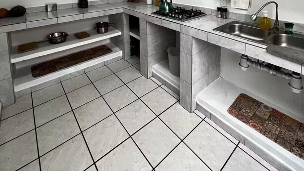 A modern kitchen with white cabinets, a stainless steel sink, and a tiled floor.