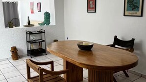 A dining area with a wooden table, two chairs, a black shelf with glassware, and a framed poster on the wall.