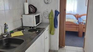 Pieni, käytännöllinen keittiö, jossa on valkoiset kaapit, mikroaaltouuni ja pesuallas. Seinällä on koristeellisia lautasia ja ovessa pyyhe.