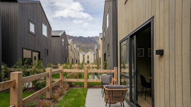 A modern building with a wooden fence, a paved patio, and a chair.