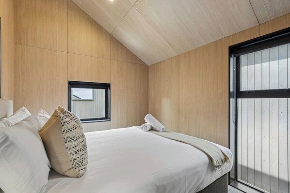 A modern bedroom with a large bed, a small window, and a balcony.