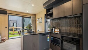 A modern kitchen with a built-in oven, a microwave, and a coffee machine. There is a dining area with a table and chairs visible through a glass door.