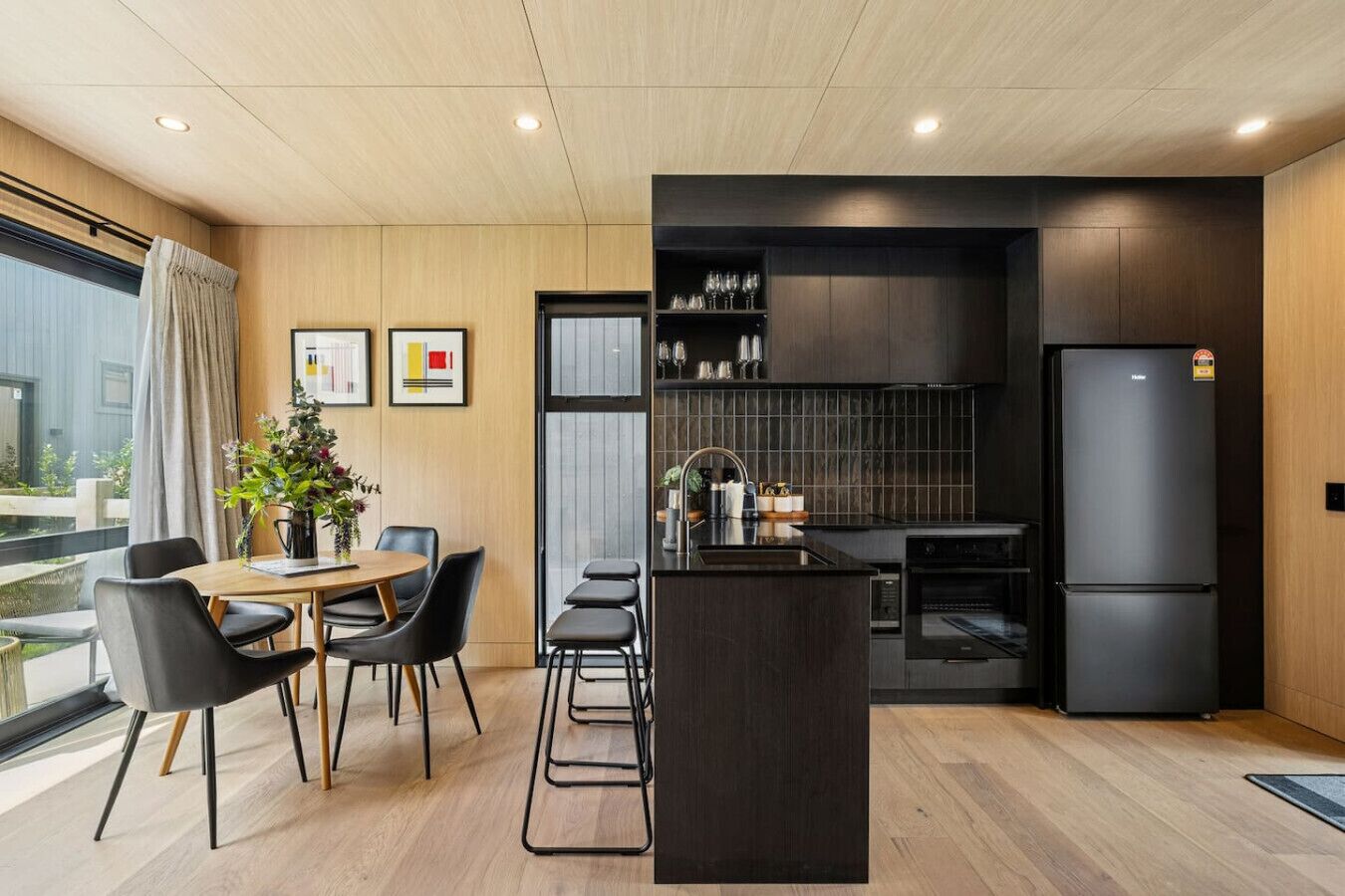 A modern kitchen with a central island, black appliances, and a dining area with a table and chairs.