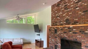 Una sala de estar con chimenea de ladrillo, un sofá blanco, un sofá rojo y un televisor de pantalla plana montado en la pared.