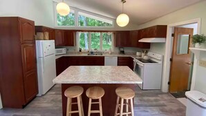 Una cocina con armarios de madera, encimera de granito, una isla integrada con taburetes e iluminación colgante.