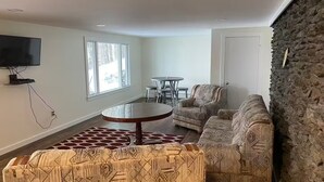 Una sala de estar con una mesa redonda, dos sillones estampados, un televisor y una pared de acento de piedra.