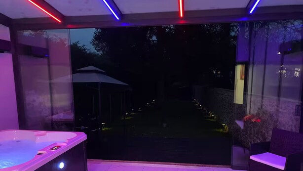 A modern outdoor patio with a hot tub, a glass door leading to a garden, and a seating area with a candle. - Private luxury suite on 2 levels (Orly-sur-Morin)