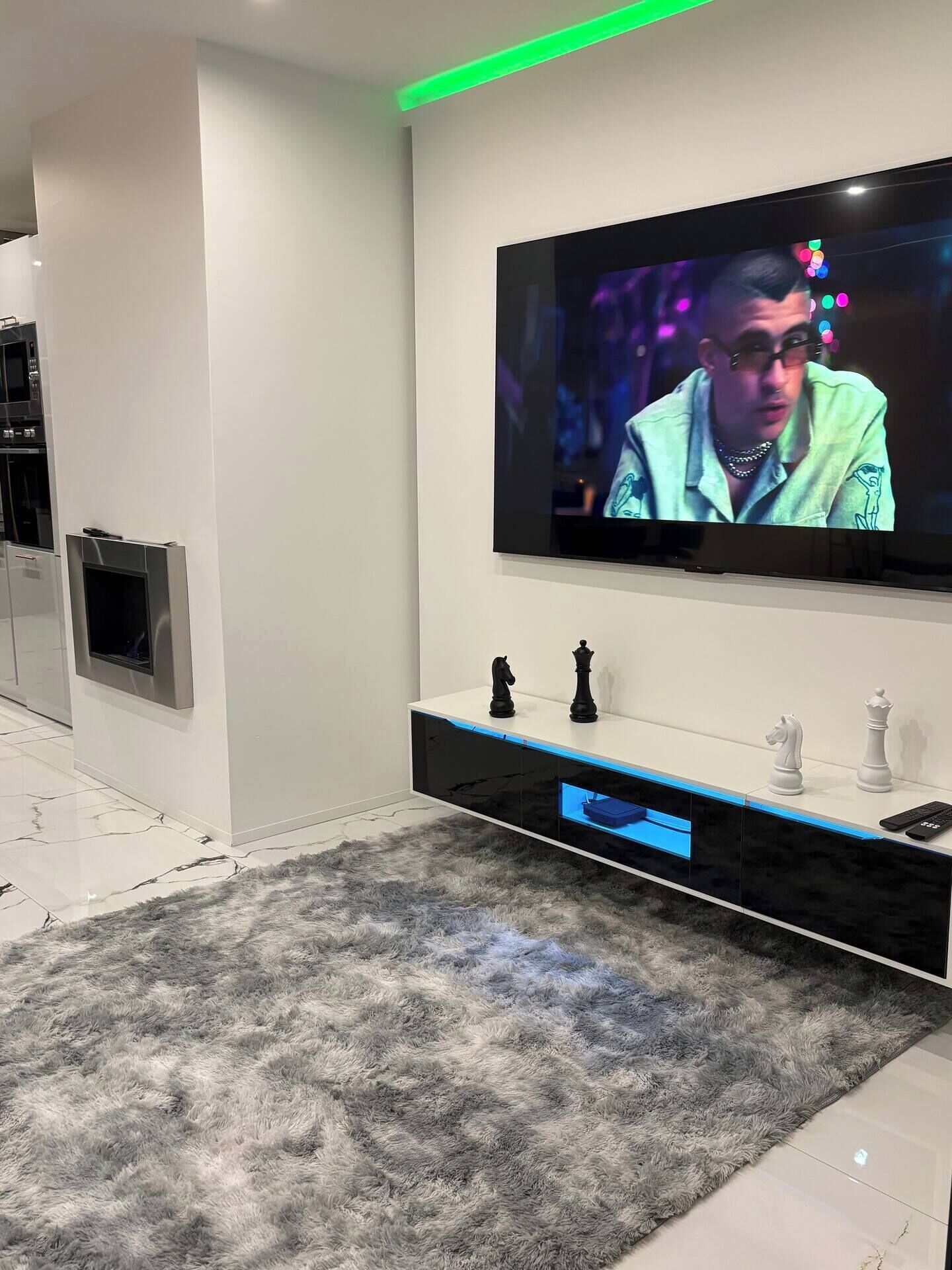 Una sala de estar moderna con un televisor de pantalla plana montado en la pared, un mueble negro para entretenimiento con piezas de ajedrez y una alfombra gris suave.