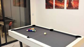 Une table de billard avec des billes, une porte en verre et deux œuvres d’art encadrées accrochées au mur.