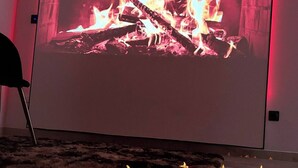A room with a large screen displaying a fire, a black chair, and candles on the floor. - Private luxury suite on 2 levels (Orly-sur-Morin)