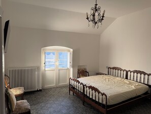 A bedroom with a large bed, a chair, a radiator, and a door with windows. - Villa Camelia: apartment with sea view (San Lorenzo della Costa)