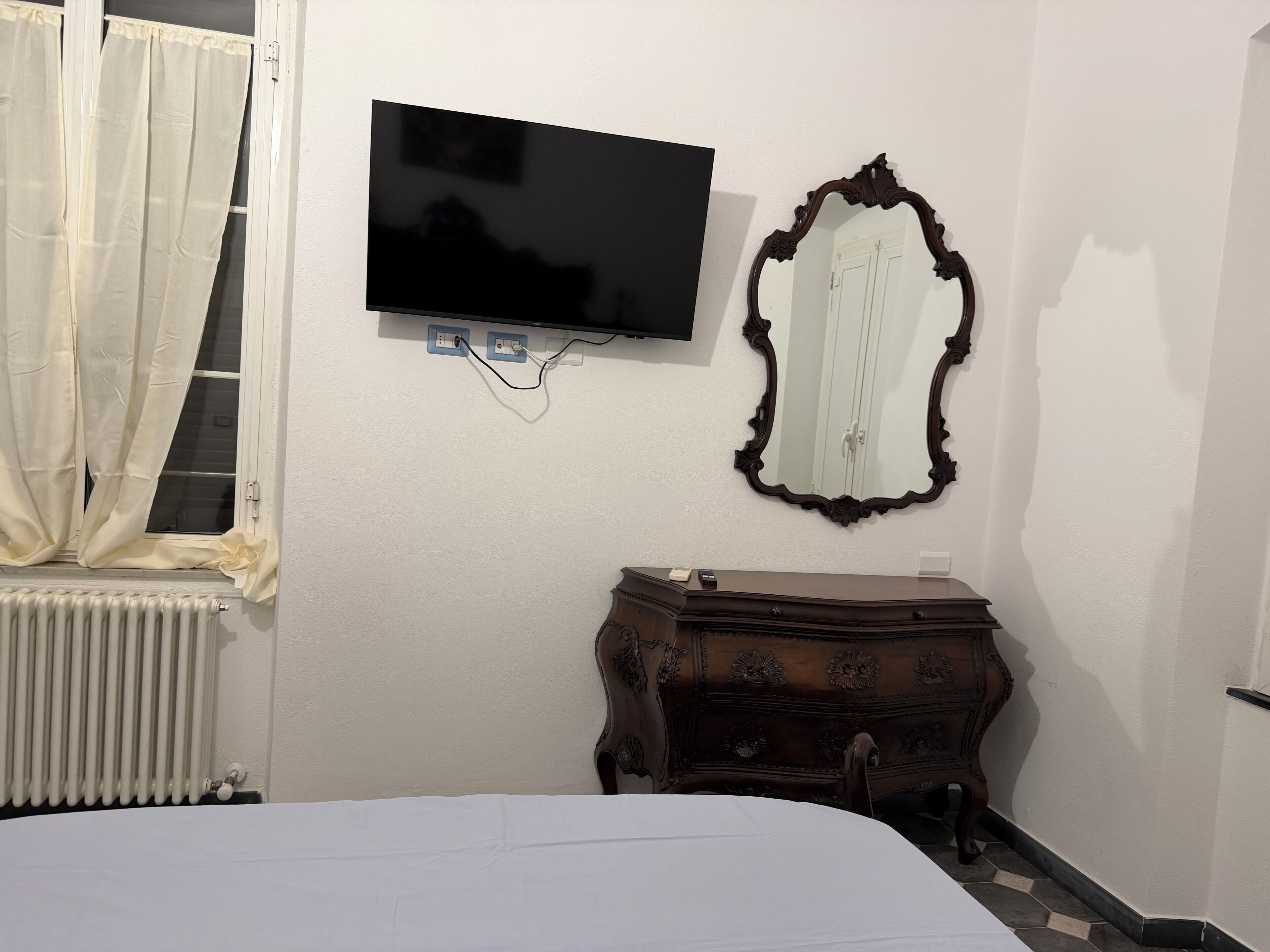 A bedroom with a bed, a dresser, a television mounted on the wall, and a mirror.