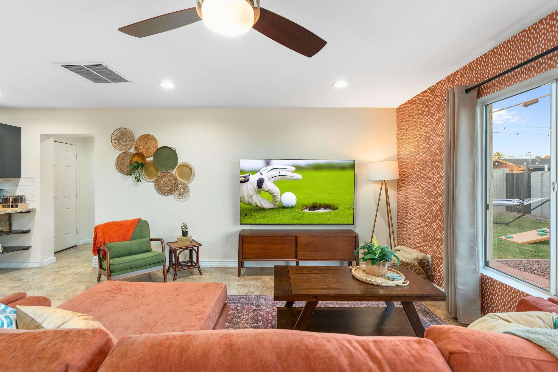 A living room with a flat-screen TV, a ceiling fan, and a large window.