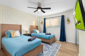 Ein Hotelzimmer mit zwei Betten, einem Deckenventilator, einem Fenster mit Vorhängen und einem gemusterten Teppich.