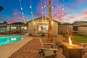 Ein Garten mit Swimmingpool, Feuerstelle und Lichterketten.
