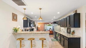 A modern kitchen with dark cabinets, a central island with stools, and pendant lighting. - Resort Pool | Private Hot Tub | Close to Old Town (Scottsdale)