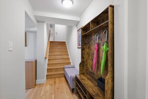 Un escalier menant à un deuxième étage, un banc en bois et un porte-manteau mural avec des crochets.