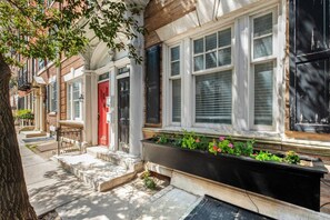 A row of townhouses with a red door, white windows, and a planter box with flowers. - Spacious 3BR Rittenhouse Retreat (Philadelphia)