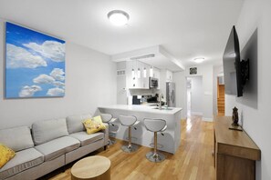 A modern apartment with a grey sofa, a kitchen island, and a TV mounted on the wall. - Spacious 3BR Rittenhouse Retreat (Philadelphia)