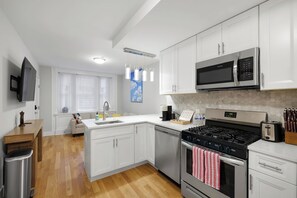 A modern kitchen with white cabinetry, stainless steel appliances, and a wooden dining table. - Spacious 3BR Rittenhouse Retreat (Philadelphia)