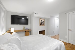 A bedroom with a bed, a TV mounted on the wall, a fireplace, and a door leading to another room. - Spacious 3BR Rittenhouse Retreat (Philadelphia)