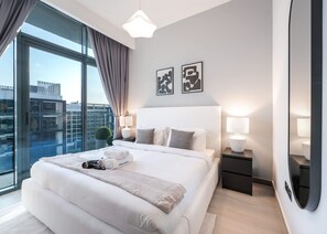 Een moderne hotelkamer met een groot bed, een nachtkastje, een lamp en uitzicht op de stad door grote ramen.