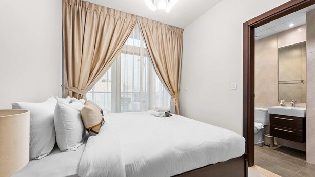 A hotel room with a large bed, a bedside lamp, and a view of the city through the window. - Stayshort - Modern Villa in Avencia Damac Hills 2 With Waterpark Access (Dubai)