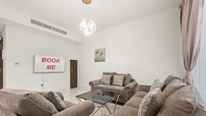 A modern living room with two sofas, a coffee table, and a TV mounted on the wall. - Stayshort - Modern Villa in Avencia Damac Hills 2 With Waterpark Access (Dubai)