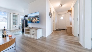Ein modernes Wohnzimmer mit Flachbildfernseher, Holzböden, einer Vitrine und einem Essbereich mit Tisch und Stühlen.