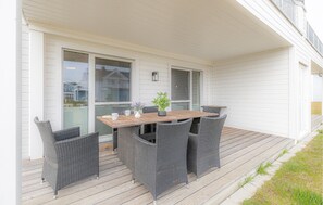 Portico esterno coperto con tavolo di legno e sedie in vimini, ampie porte scorrevoli in vetro e vista su zona residenziale.