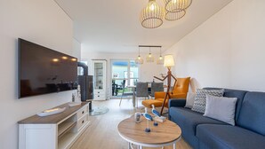 Una sala de estar moderna con un televisor de pantalla plana, una mesa de centro de madera, un sofá azul y un comedor con sillas y una mesa.
