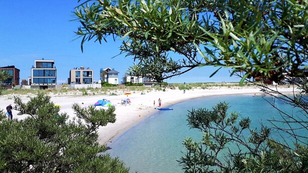 Una playa con edificios modernos, agua azul cristalina y vegetación escasa.