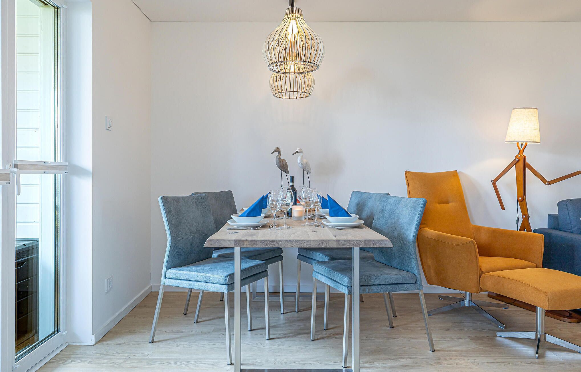 A dining area with a table set for four, surrounded by modern chairs, a chandelier, and a floor lamp.