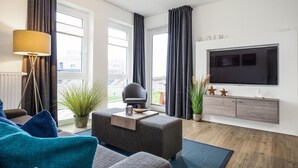 Una sala de estar moderna con un sofá, una mesita de centro, una lámpara de pie, un televisor y vistas al exterior.