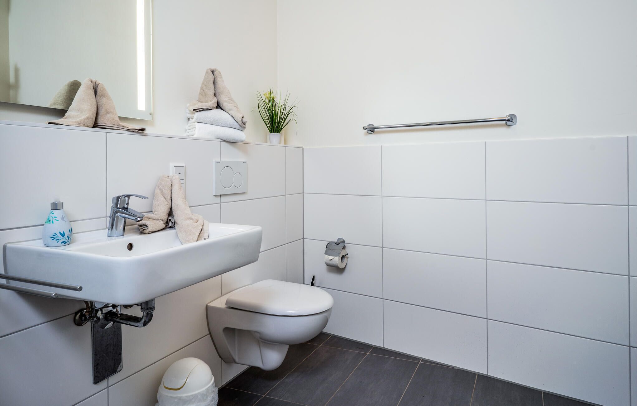 Een moderne badkamer met een wit wastafel, toilet, handdoekhouder en handdroger.