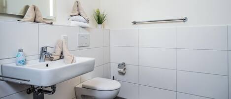 Een moderne badkamer met een wit wastafel, toilet, handdoekhouder en handdroger.