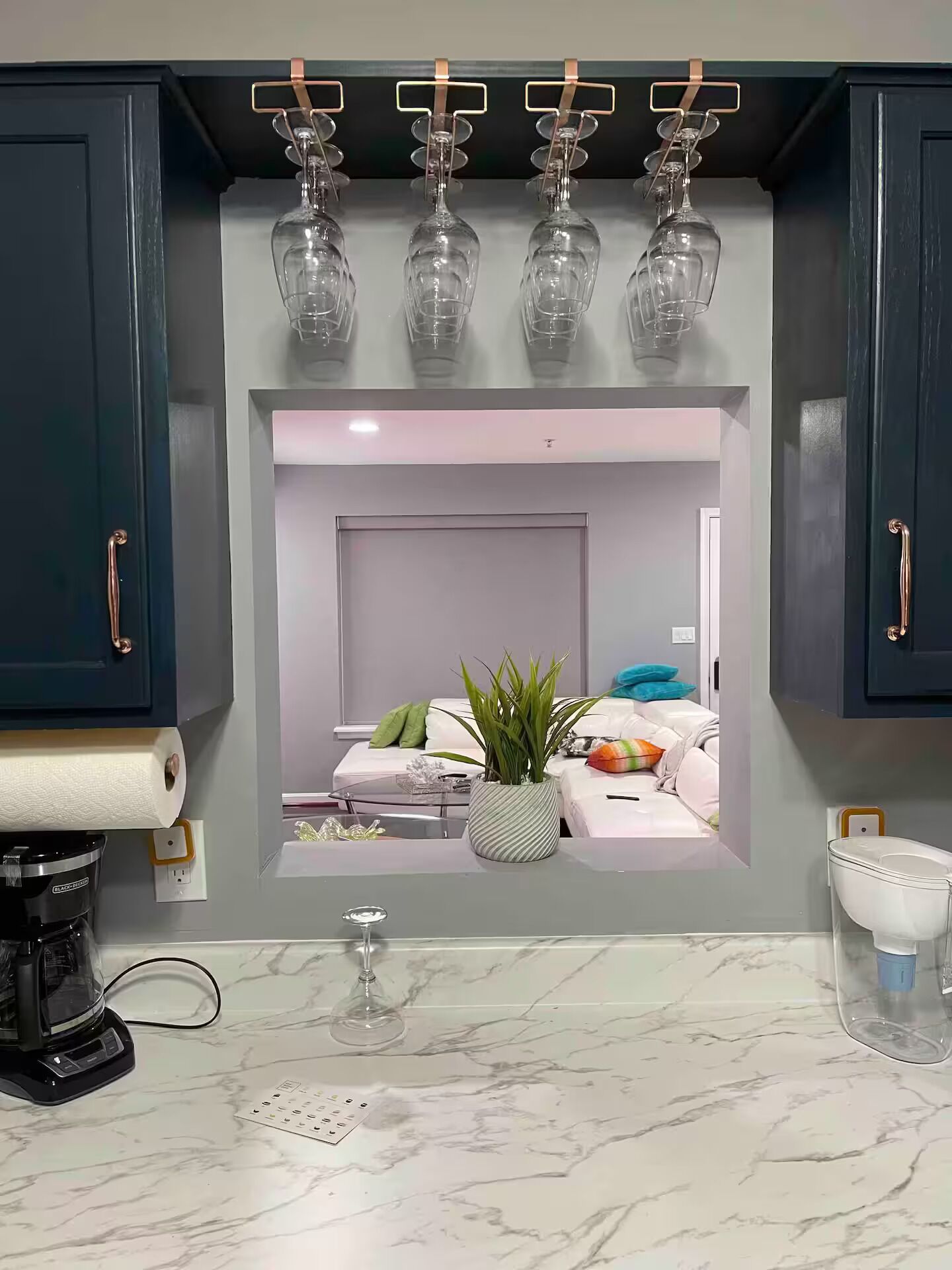 Una cocina con encimera de mármol, cafetera y copa de vino.