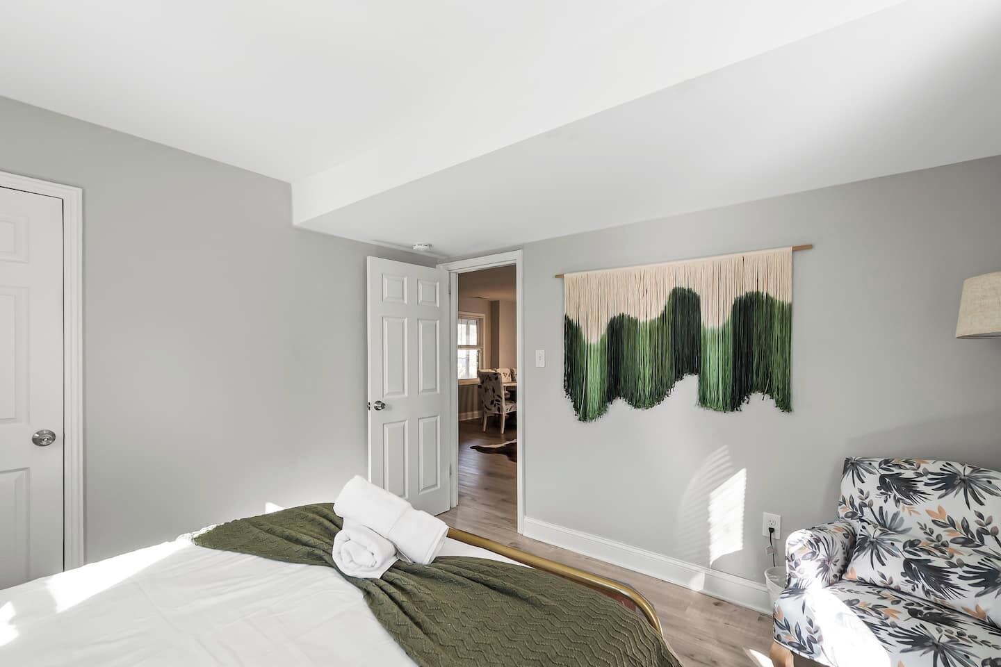 Un dormitorio con cama, una silla, un cuadro en la pared y una puerta que da a otra habitación.