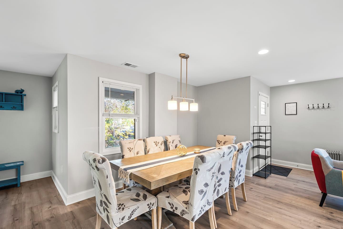A dining area with a wooden table and floral-patterned chairs, a pendant light, and a window with blinds.